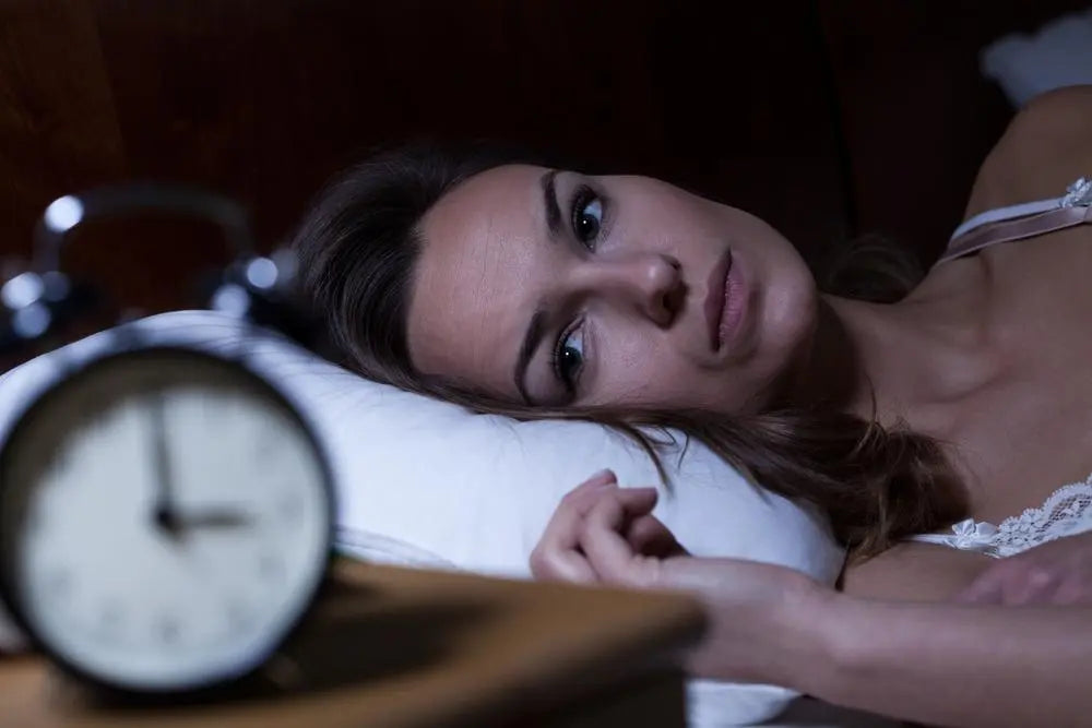 Lady lying wide awake in bed looking at her clock.