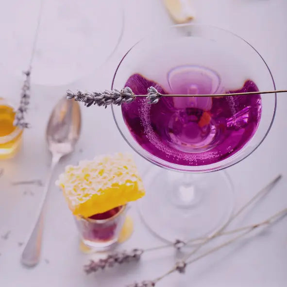Lavender syrup in a lemon drop martini with a lavender stem across the top. There is also a honeycomb and a silver spoon on the table