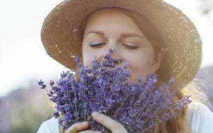 woman with a straw hat smelling a bundle of lavender