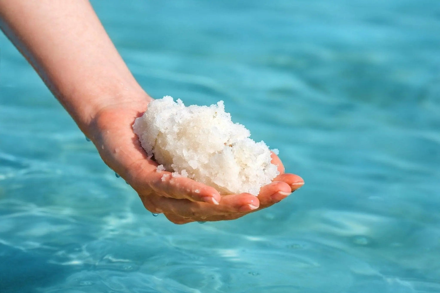 sea salts held in a hand over bright blue water