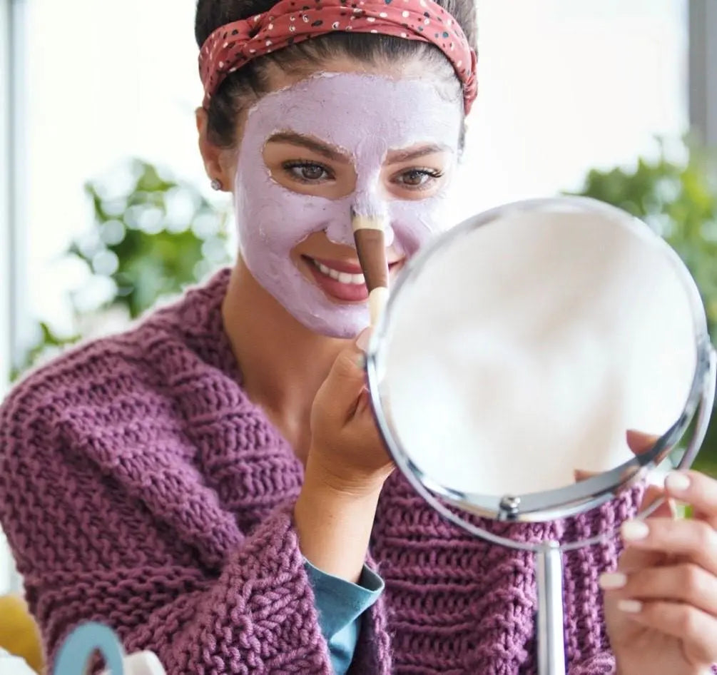 Lady placing purple skin mask on her face with a brush