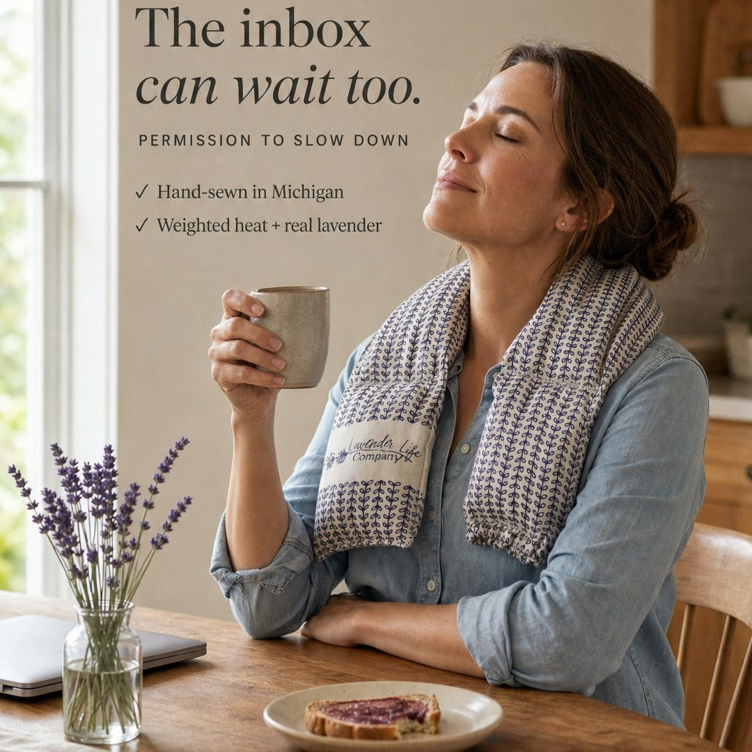 A woman sits at a wooden table in a warm kitchen setting, holding a mug with a knitted lavender-themed neck warmer draped around her shoulders. Text on the left reads, 'The inbox can wait too.