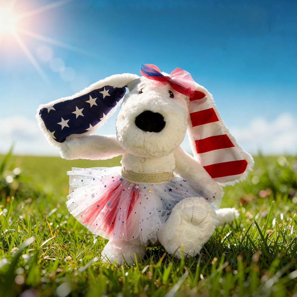 Plush dog toy with American flag design sitting on grass with a blue sky background